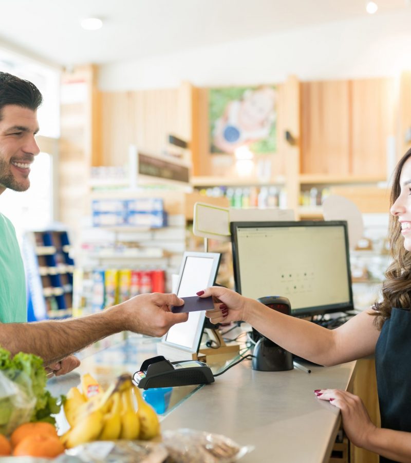 Smiling female cashier with buyer at checkout counter in grocery store