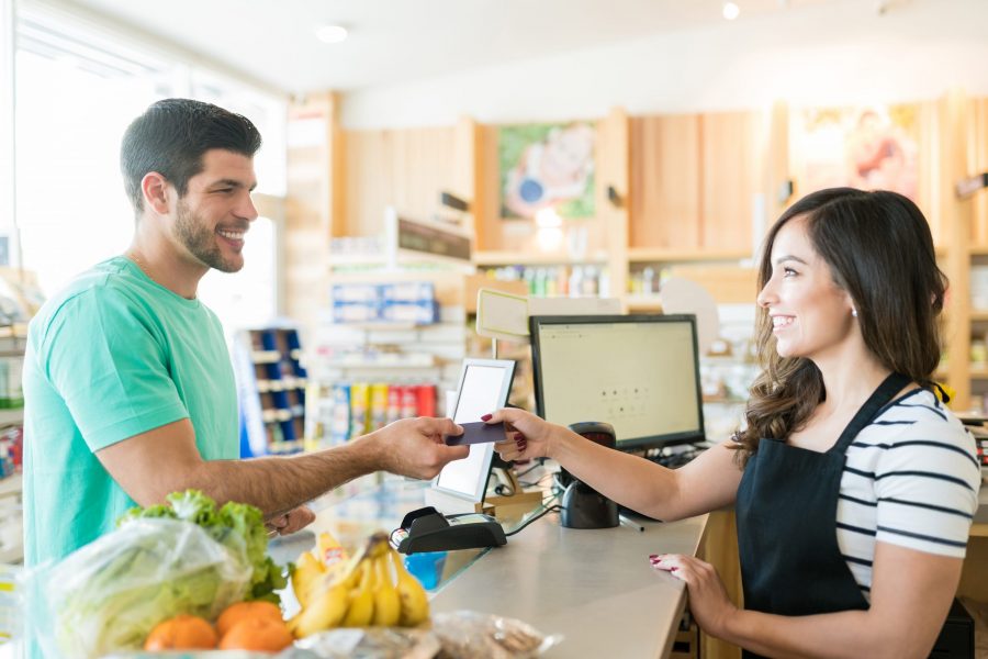 Smiling female cashier with buyer at checkout counter in grocery store